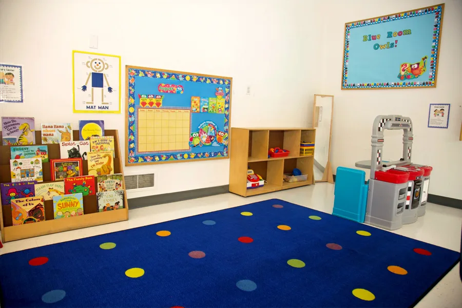 The Blue Room: a picture book display, a bulletin board reading Blue Room Owls, low shelving with a toy kitchen, and a navy rug with colored spots.