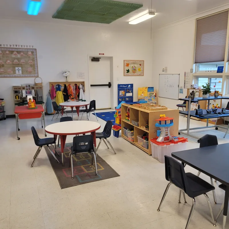 A classroom corner with dress-up clothes on hooks, a play kitchen, a small round table and a hopscotch rug.